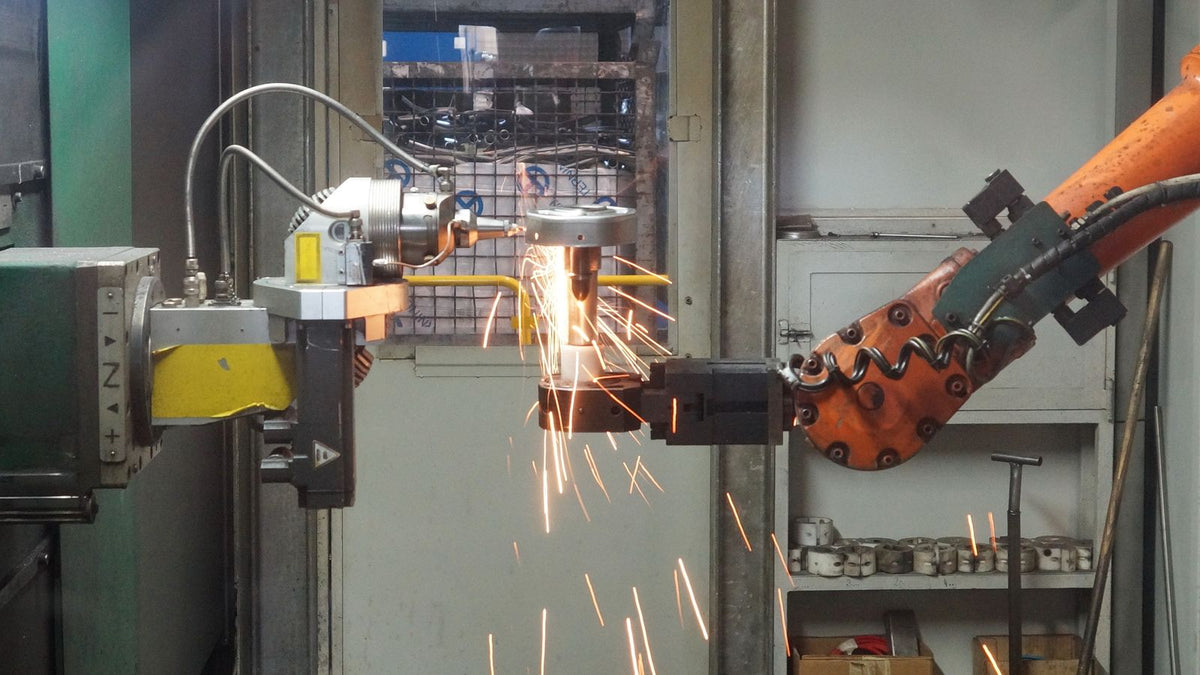 A robotic arm grinding a metal workpiece on a factory floor, with sparks flying off the surface.