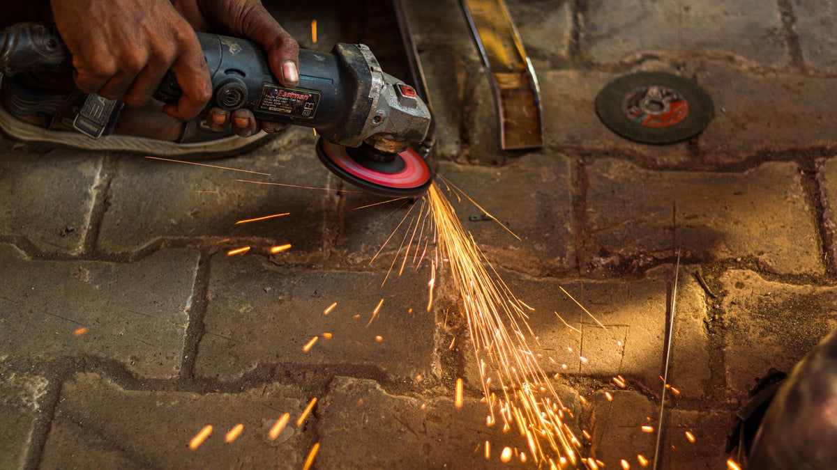 Worker using an angle grinder with a cutting disc on a steel workpiece, sparks flying in a fabrication shop