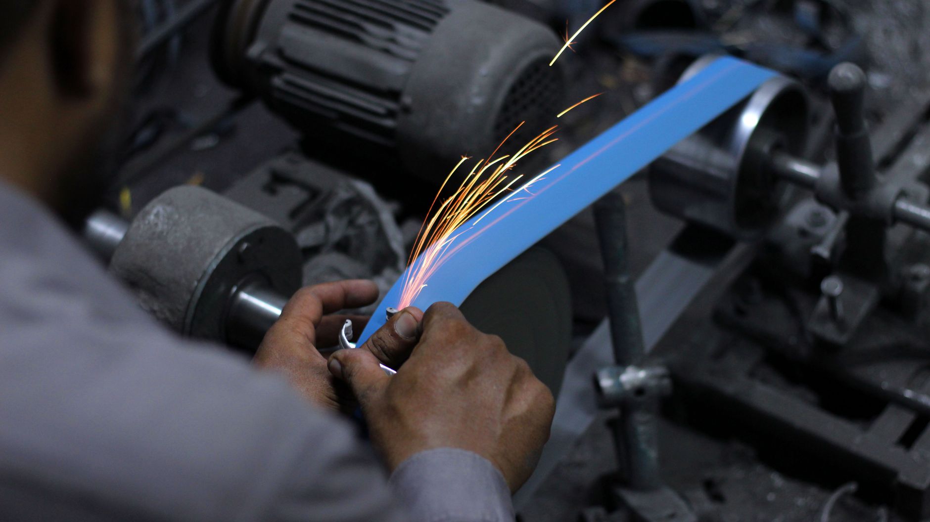 Belt grinder throwing sparks while grinding a steel workpiece in a metal fabrication shop