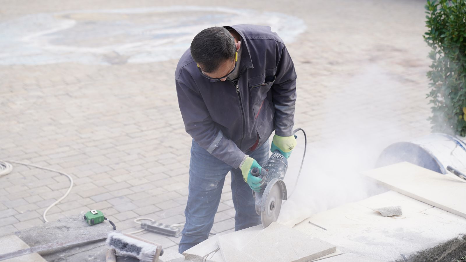 Worker using a handheld concrete saw with visible dust while cutting on a job site