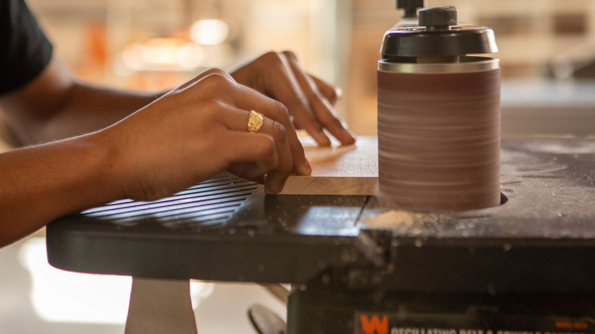Worker running a metal workpiece through a belt sanding machine in a fabrication shop