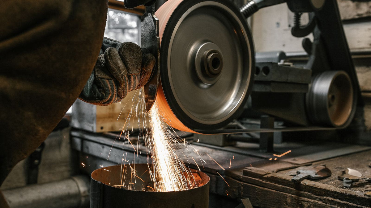 Fabricator cutting a steel bar with an angle grinder in a metal fabrication shop, sparks flying