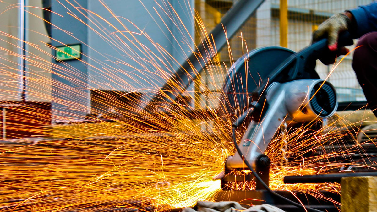 A worker using an angle grinder with a flap disc to finish a metal weld, sparks flying in a fabrication shop