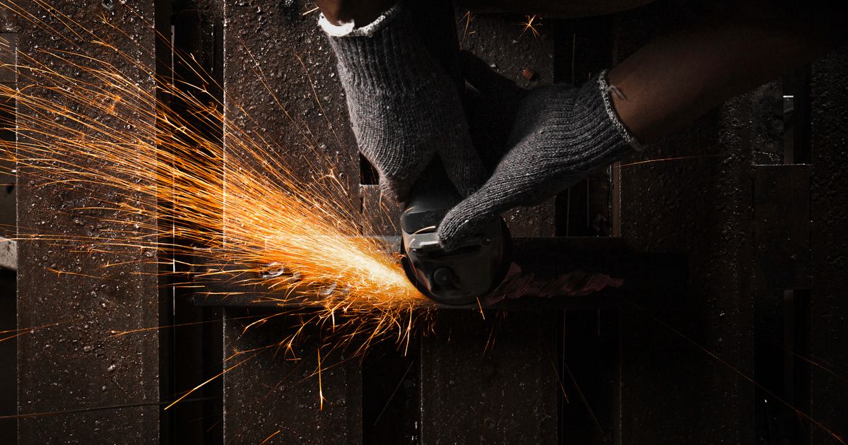 An industrial worker grinding metal with an angle grinder, sparks flying — how to remove mill scale from steel, Whitby Abrasives, Ontario, Canada