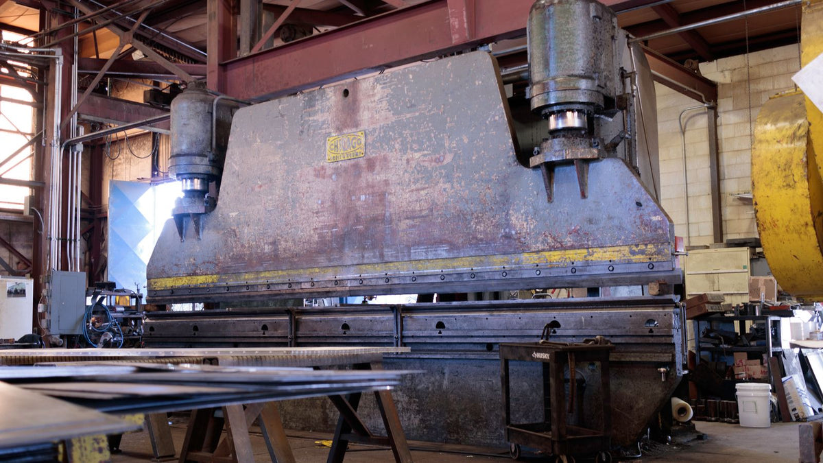 A machinist grinding a steel workpiece on a busy metal fabrication shop floor, sparks flying