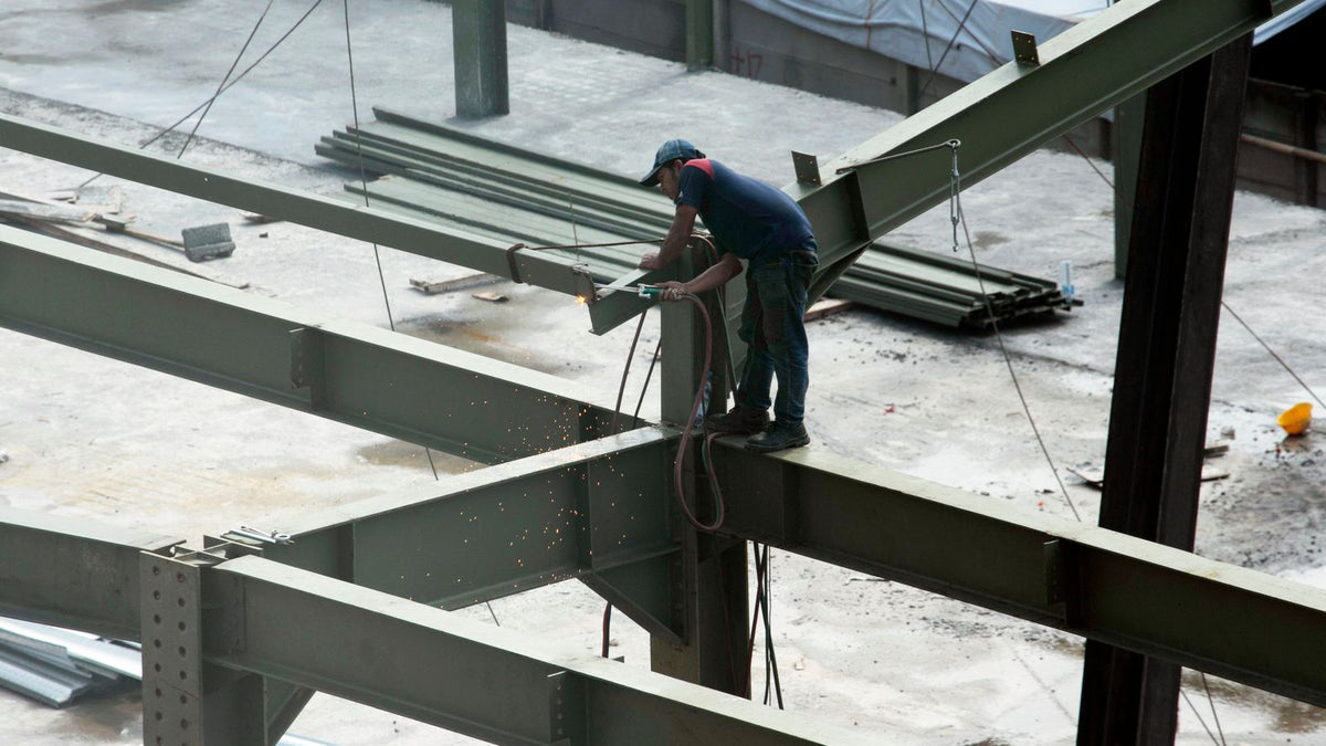Ironworkers welding and grinding structural steel beams at a large construction site