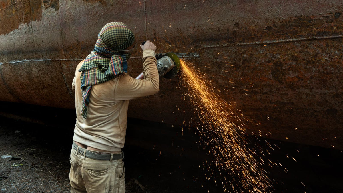 A welder grinding a weld seam on a large steel pipe at an outdoor pipeline construction site.
