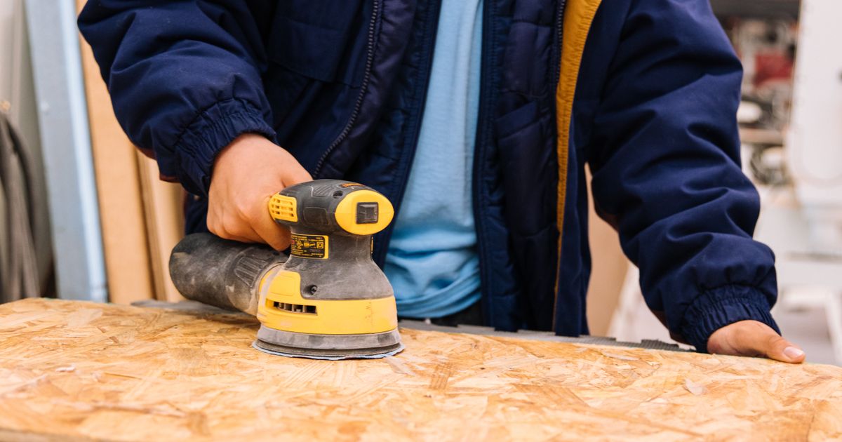 A worker sanding a board with a power sander in a workshop — sanding belt selection, Whitby Abrasives, Ontario, Canada