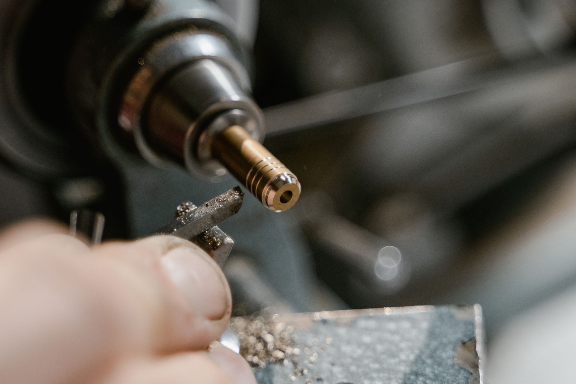 Machinist hand-polishing a turned steel shaft on a manual lathe with a strip of cloth-backed abrasive