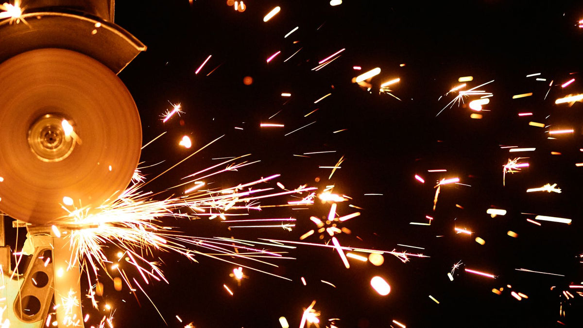 A technician grinding an aluminum workpiece with an angle grinder in a metal fabrication shop.