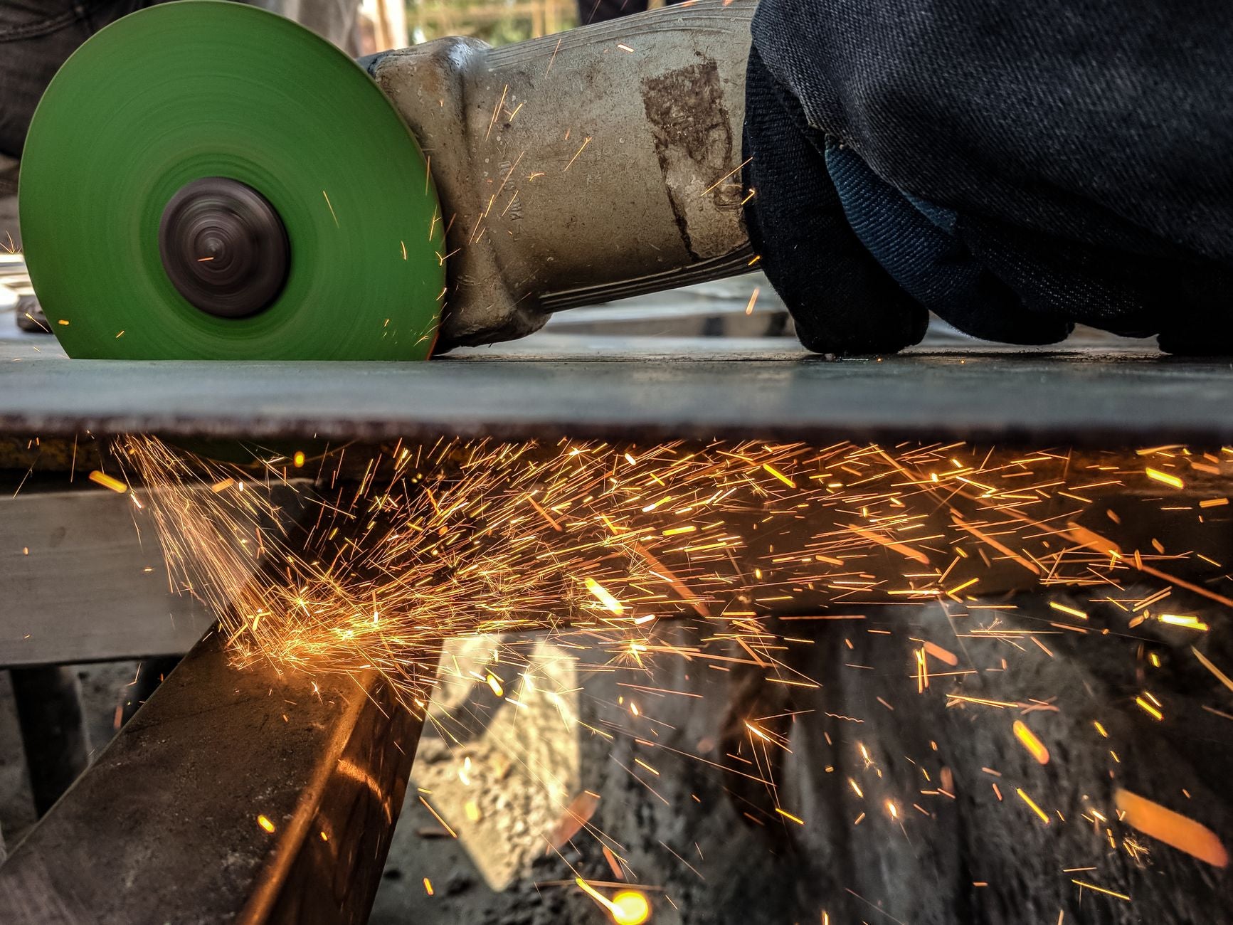 Worker in gloves grinding steel with an angle grinder, sparks flying from the disc