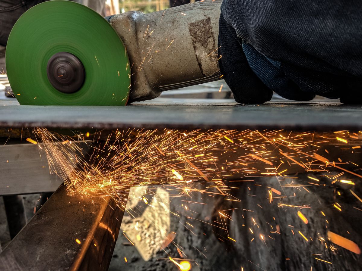 A metalworker using an angle grinder on steel, throwing sparks in a workshop